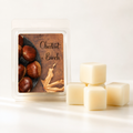 A wax melt package labeled 'Chestnut + Birch' stands next to four pale cream wax cubes on a clean white background. The package shows chestnuts and a leaf illustration.