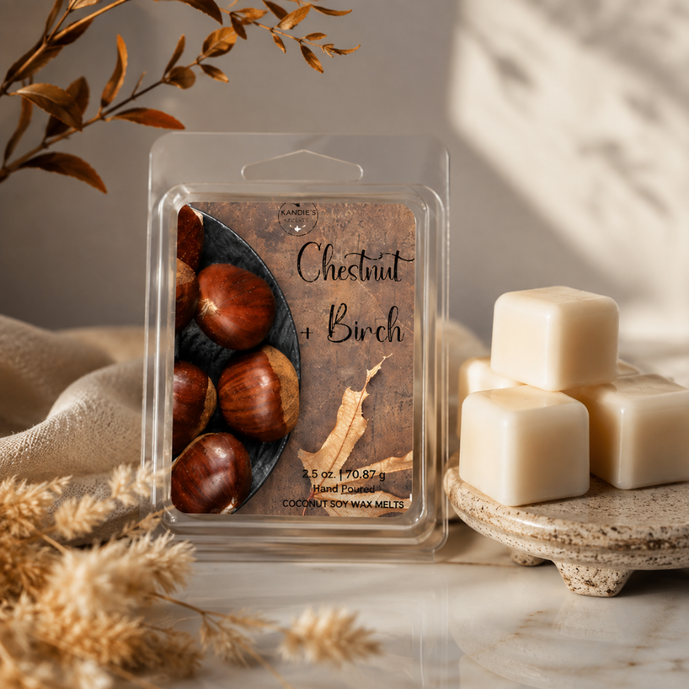 A clear plastic clamshell package labeled 'Chestnut + Birch' containing 100% soy wax melts, styled on a marble surface with cream wax cubes, dried grasses, and warm natural shadows.