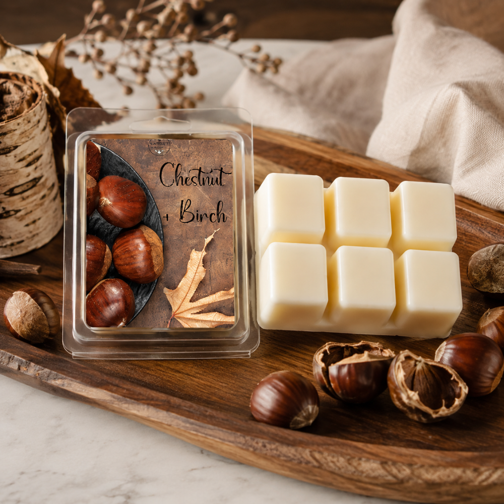 A packaged wax melt set labeled 'Chestnut & Birch' sits on a wooden board beside six cream-colored wax cubes. The scene includes chestnuts, dried leaves, a burlap cloth, and a birch tree trunk, creating a rustic autumn styling.