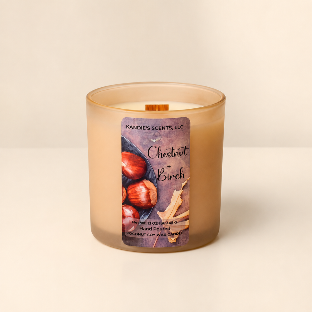 A frosted glass jar candle with a warm beige-tan wax body and a front label reading 'Chestnut + Birch' by Kandie's Scents. The candle is photographed on a clean off-white surface against a matching light neutral background.