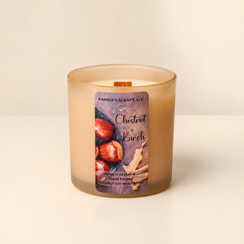 A frosted glass jar candle with a warm beige-tan wax body and a front label reading 'Chestnut + Birch' by Kandie's Scents. The candle is photographed on a clean off-white surface against a matching light neutral background.