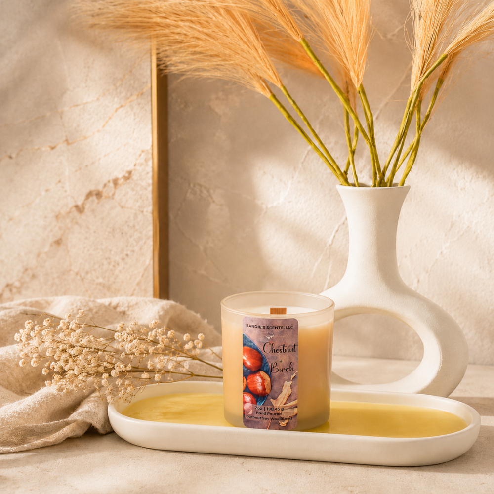 A lit scented candle in a tan glass jar sits on a white tray in a styled interior scene. 