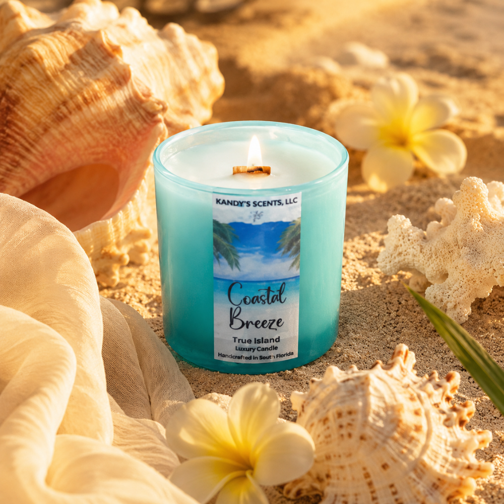 Candle labeled 'Coastal Breeze' surrounded by seashells and flowers on sand
