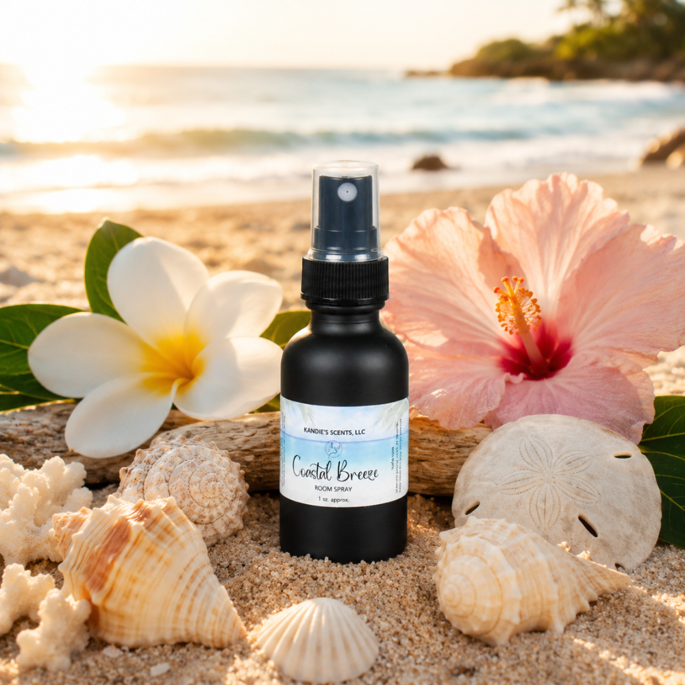 Bottle of 'Coastal Breeze' body spray on a sandy beach with flowers and shells.