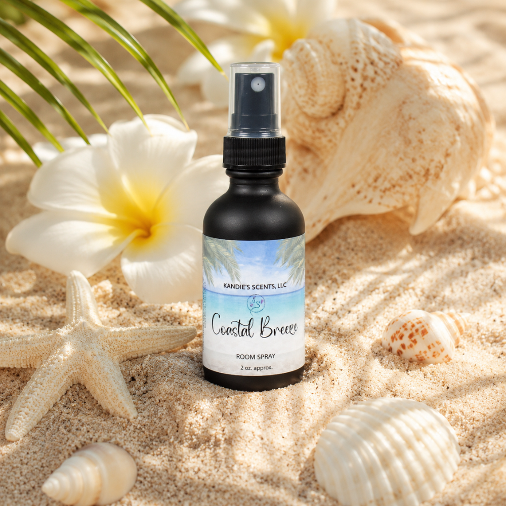 Room spray bottle labeled 'Coastal Breeze' on sand with shells and flowers