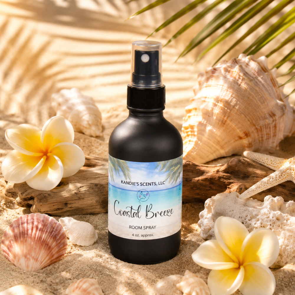 Room spray bottle labeled 'Coastal Breeze' surrounded by seashells and flowers on a sandy background.