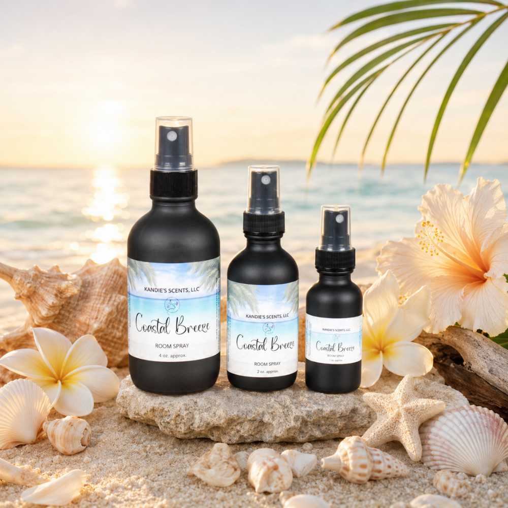 Three bottles of 'Coastal Breeze' room spray on a beach setting with flowers and shells.