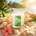 Candle labeled 'Dewy Mornings' on a sandy beach with flowers and shells