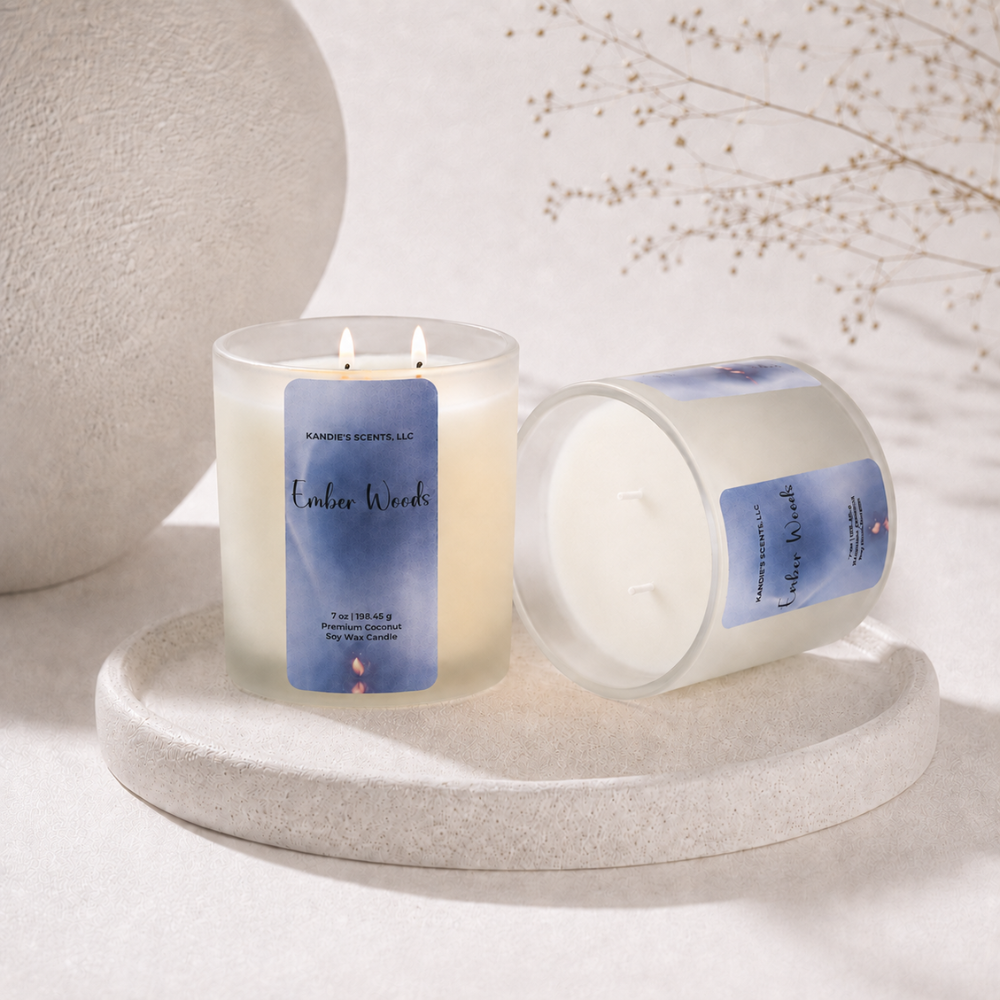 Two double-wick soy candles in frosted glass jars with blue and white labels reading 'Ember Woods' by Kandie's Scents, styled on a round stone tray with dried floral decor in the background.