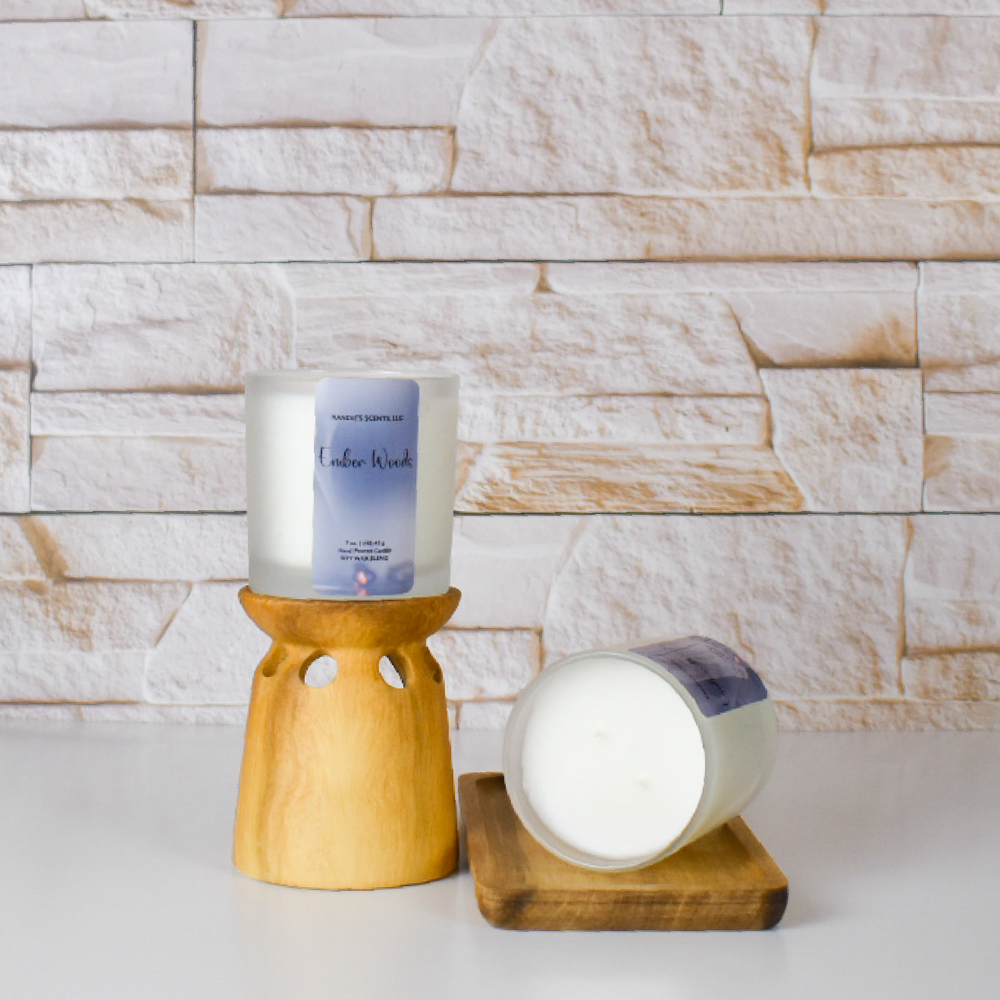 A white wax candle in a frosted glass jar with a lavender-themed label, shown on a wooden scented candle holder and lying on a small wooden tray, set against a light stone-tile wall background.