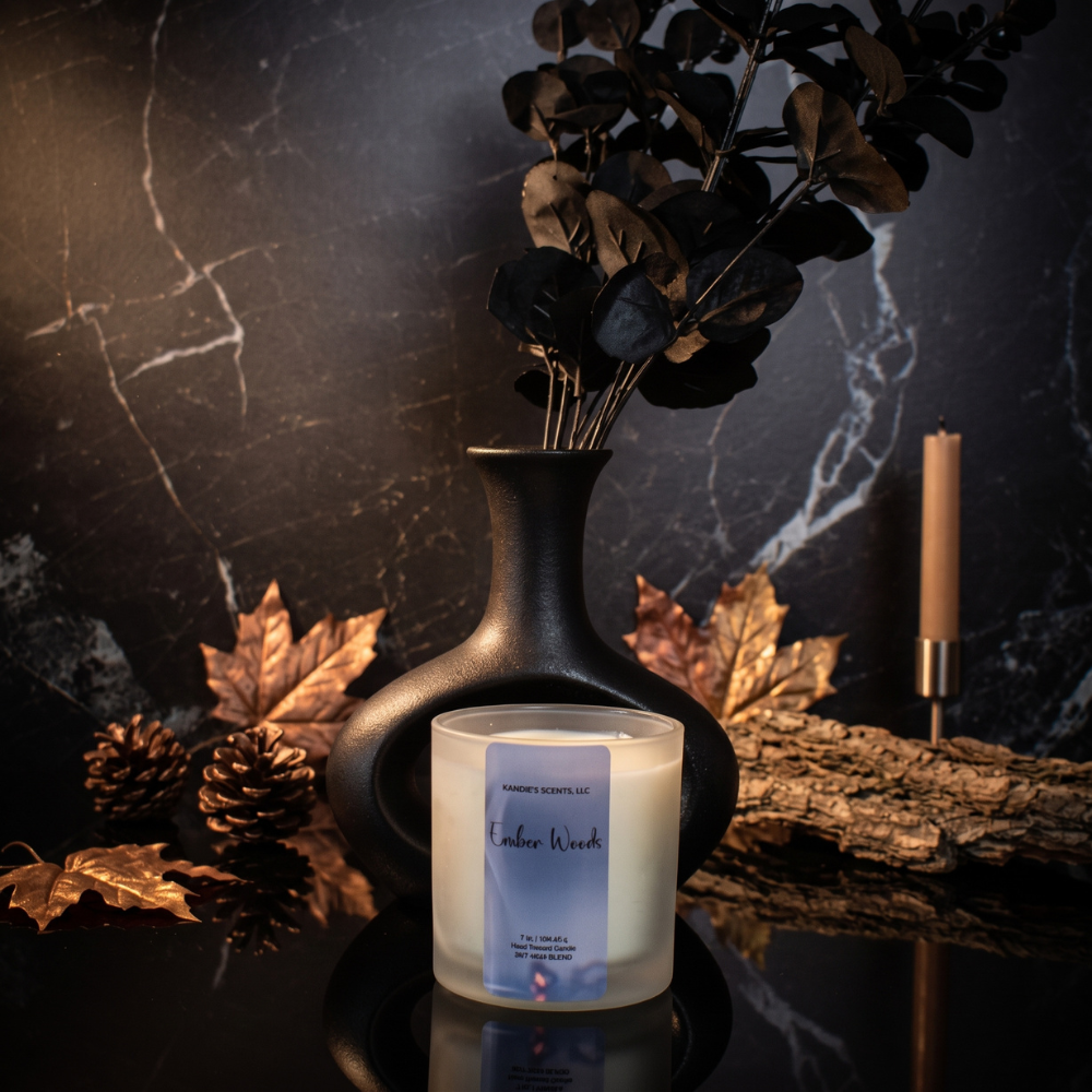 A scented candle in a frosted glass jar sits on a dark reflective surface in a styled setting. 