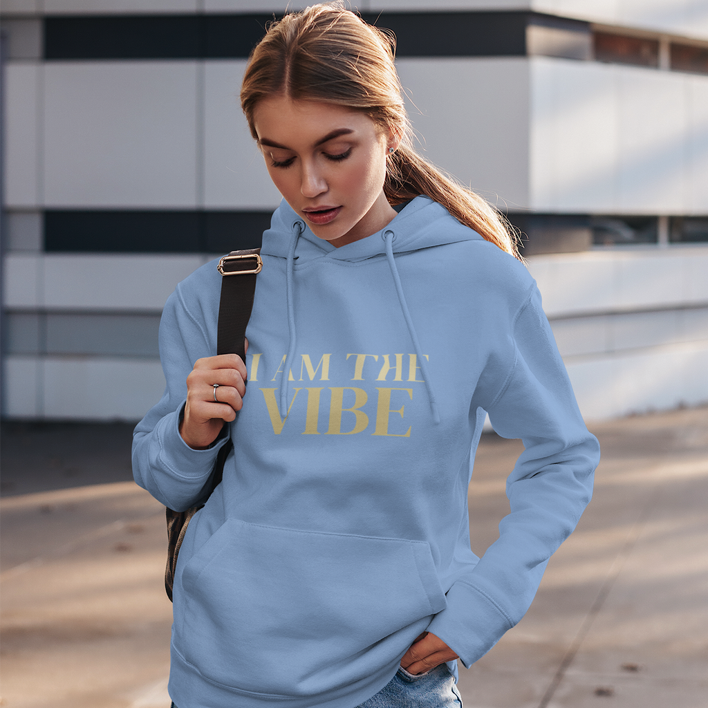 Woman wearing a blue hoodie with 'I AM THE VIBE' text, standing outdoors.
