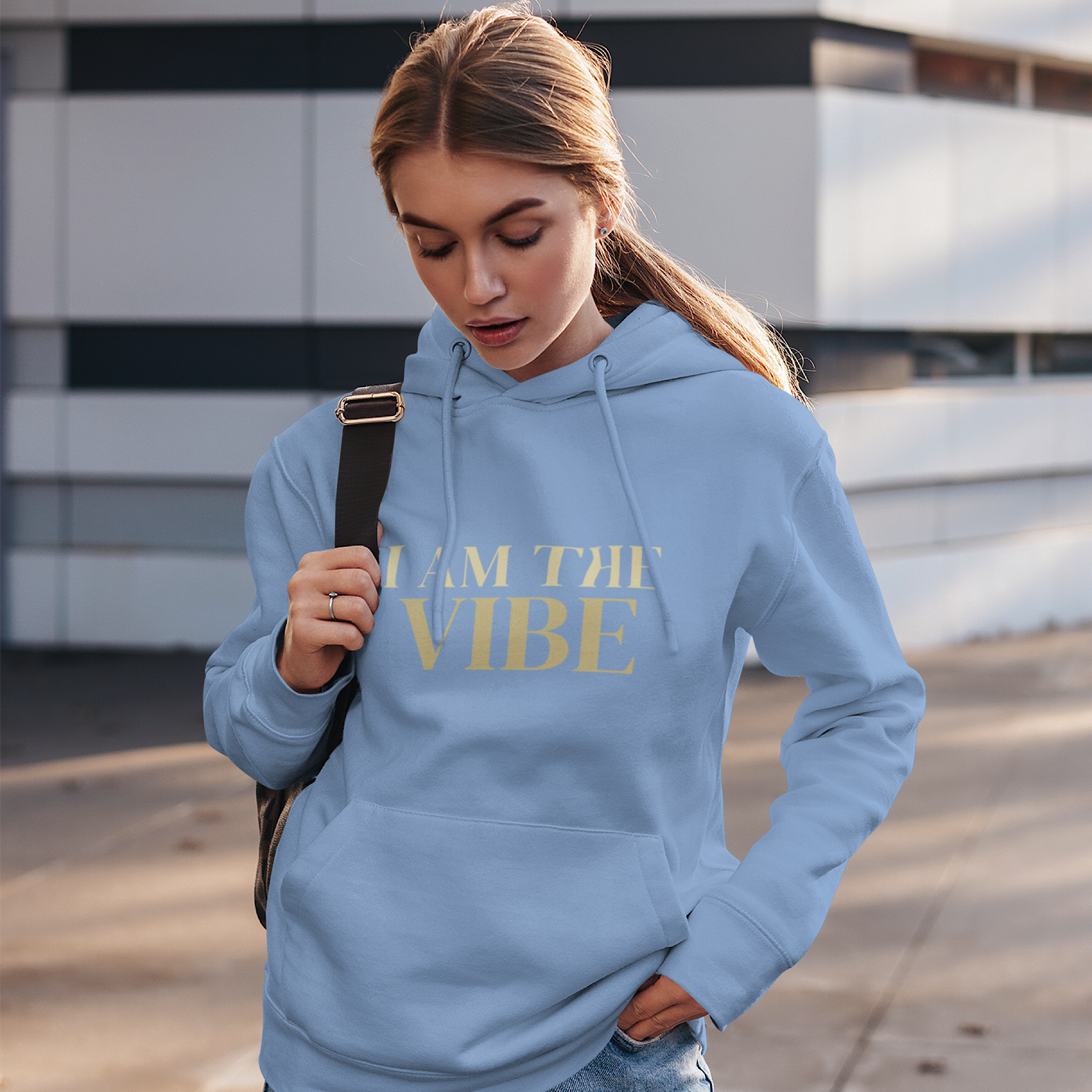 Woman wearing a blue hoodie with 'I AM THE VIBE' text, standing outdoors.
