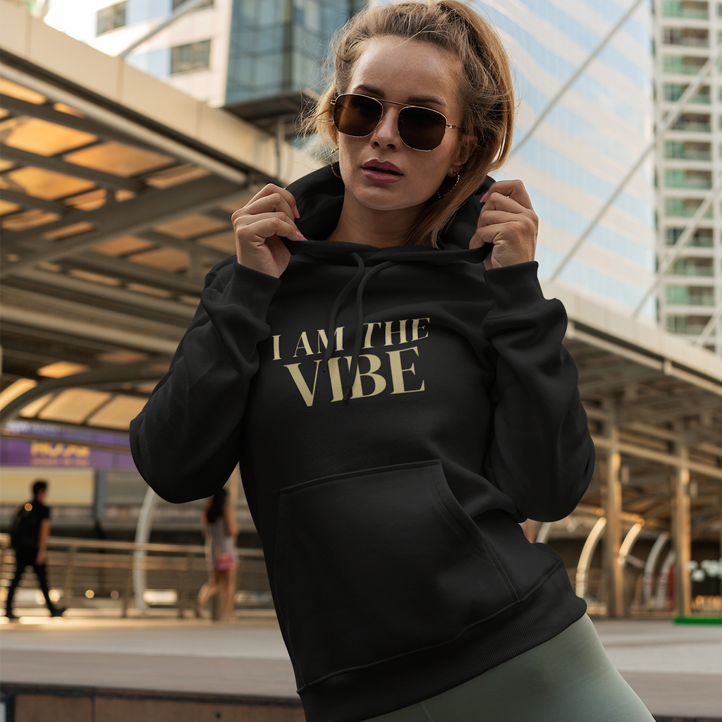 Woman wearing a black hoodie with 'I AM THE VIBE' text in an urban setting