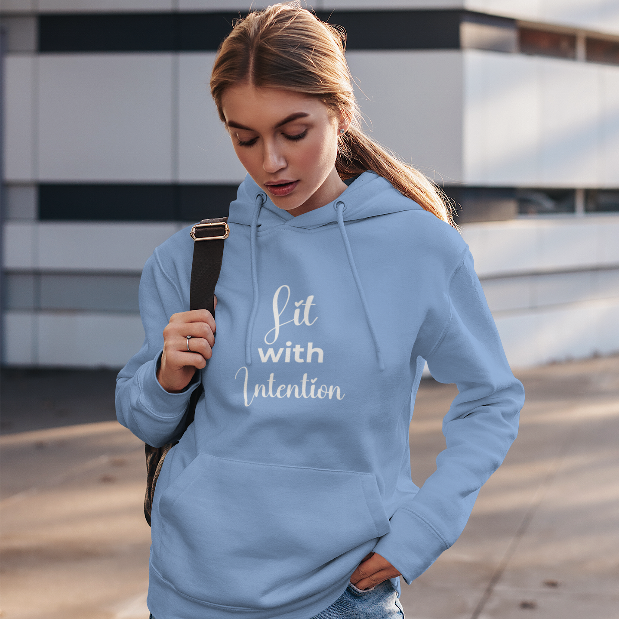 Woman wearing a light blue hoodie with 'Lit with Intention' text, standing outdoors.