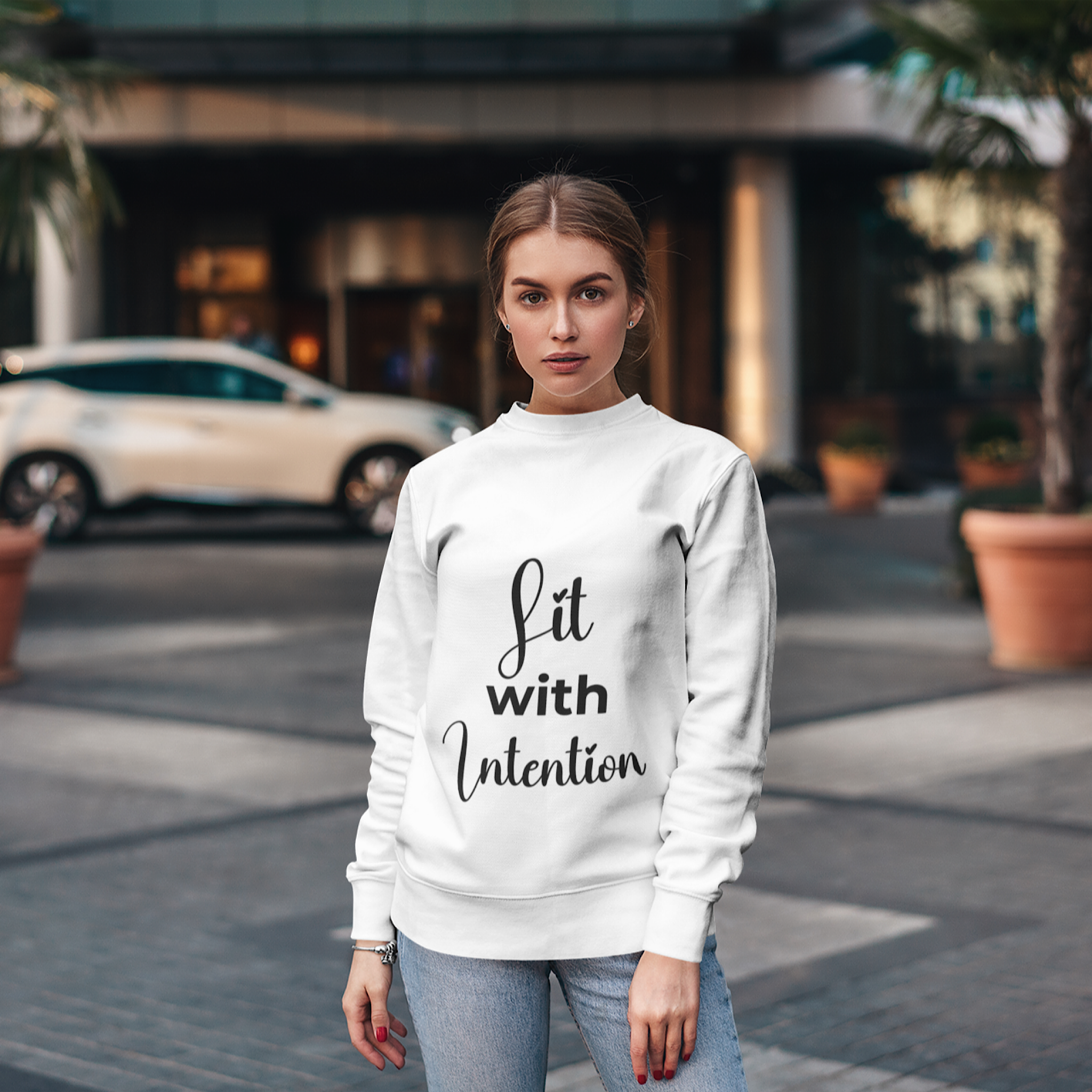Woman wearing a white sweatshirt with 'Lit with Intention' text, standing on a street.