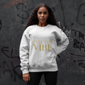 Woman wearing a white sweatshirt with 'I AM THE VIBE' text in gold against a graffitied wall.