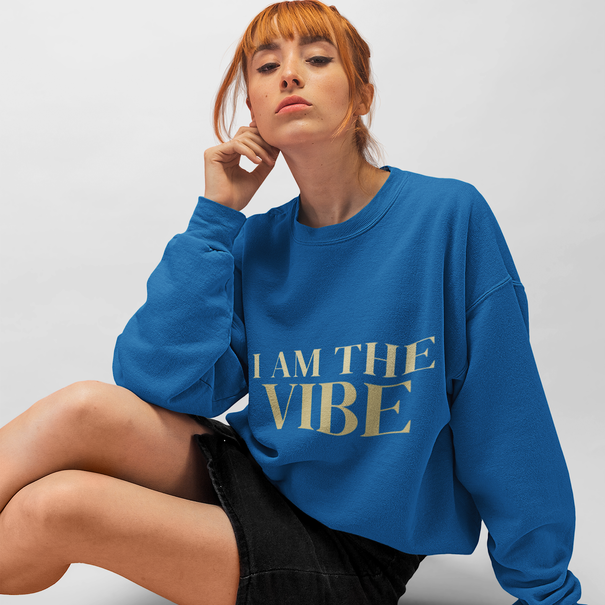 Woman wearing a blue sweatshirt with 'I AM THE VIBE' text on a plain background