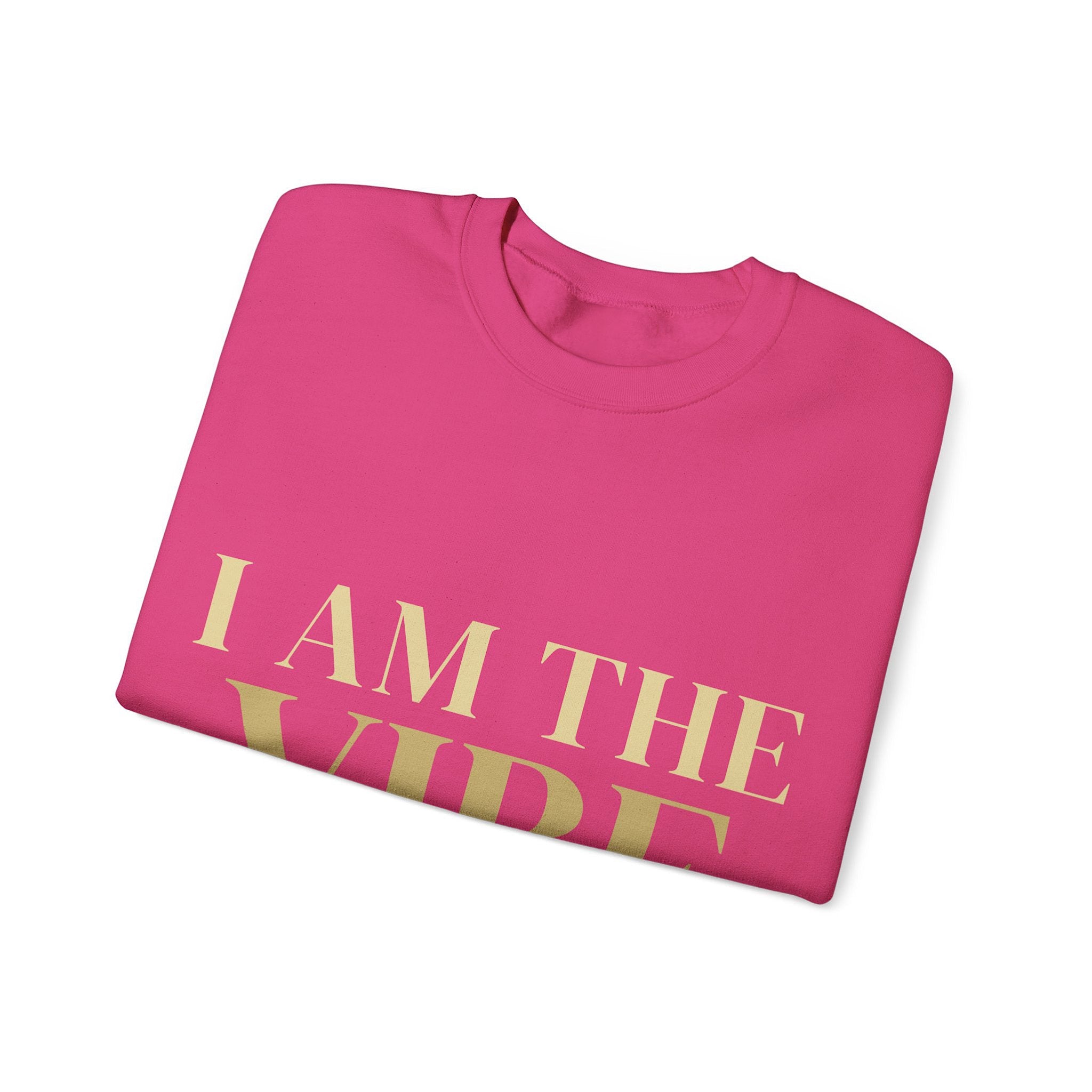 Folded pink sweatshirt with 'I AM THE VIBE' text in gold on a white background
