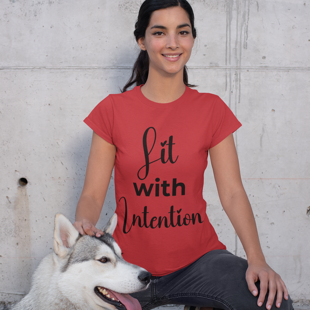 Woman wearing a red t-shirt with 'Lit with Intention' text, sitting next to a dog against a concrete wall.