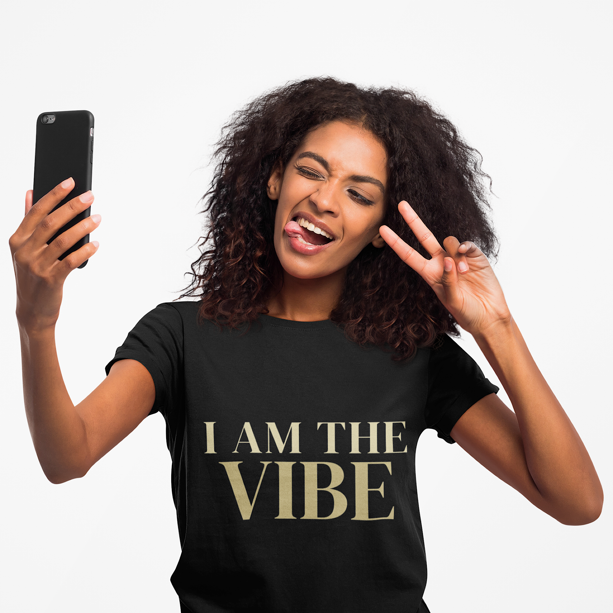 Woman wearing a black t-shirt with a 'I AM THE VIBE' design, holding a phone and making a peace sign.