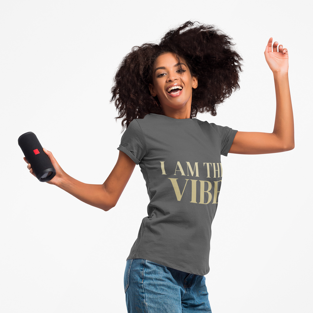 Woman wearing a gray t-shirt with 'I AM THE VIBE' text, holding a black speaker.