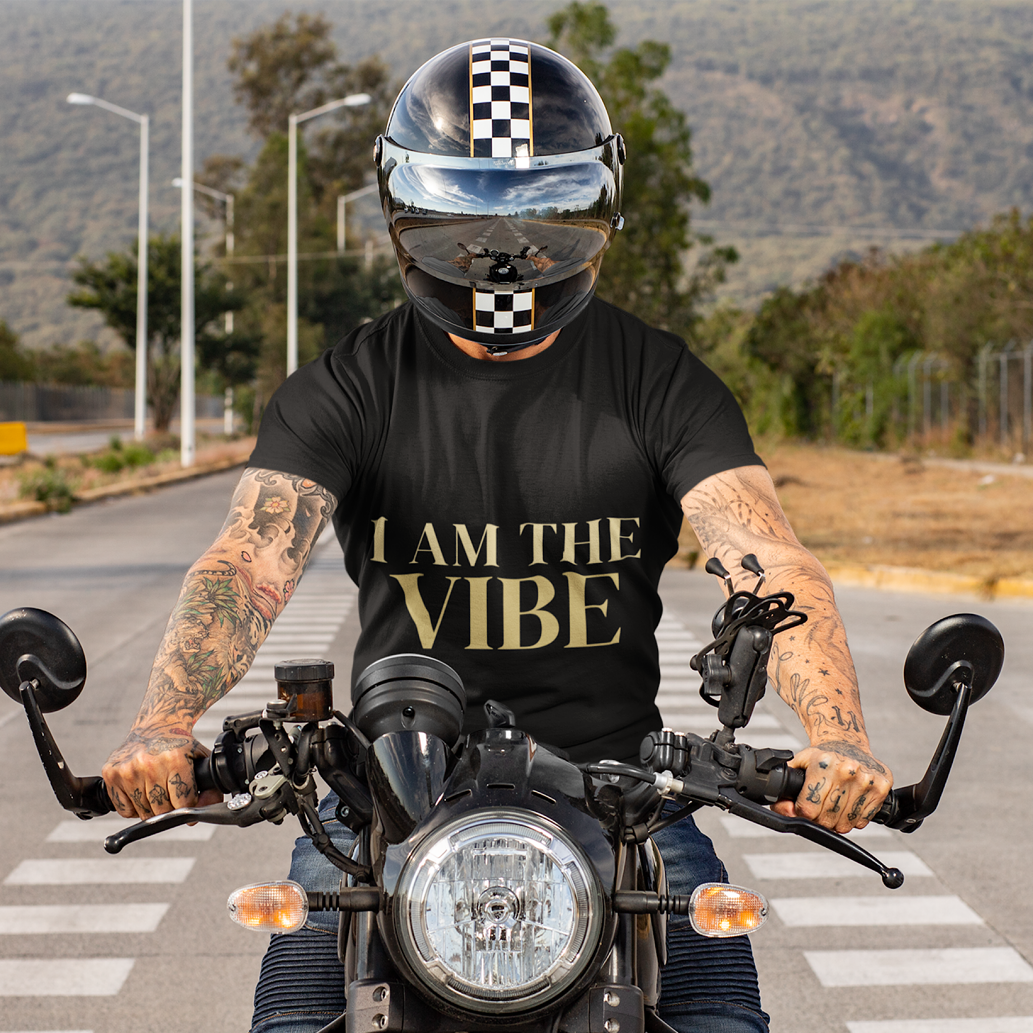 Person on a motorcycle wearing a black t-shirt with 'I AM THE VIBE' text, checkered helmet.