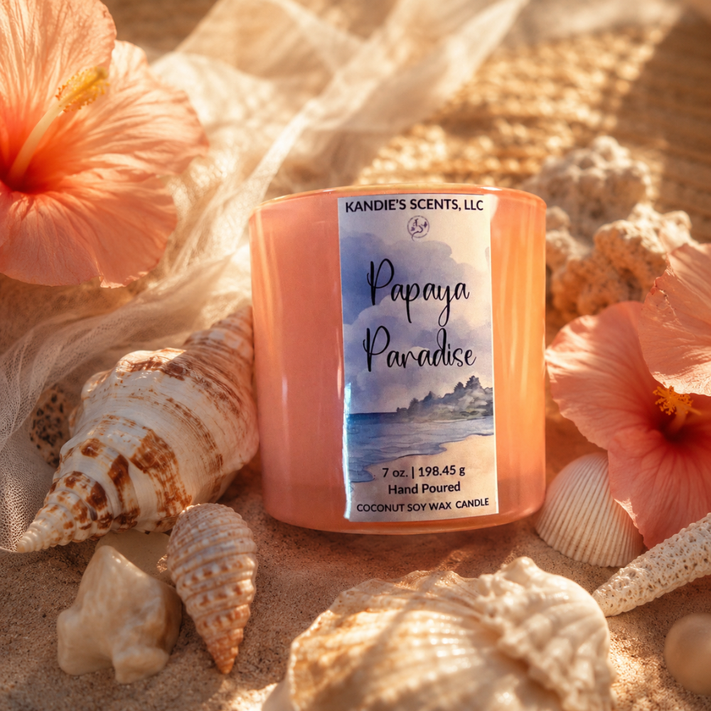 Candle labeled 'Papaya Paradise' by Kandie's Scents, LLC surrounded by seashells and flowers on sand.