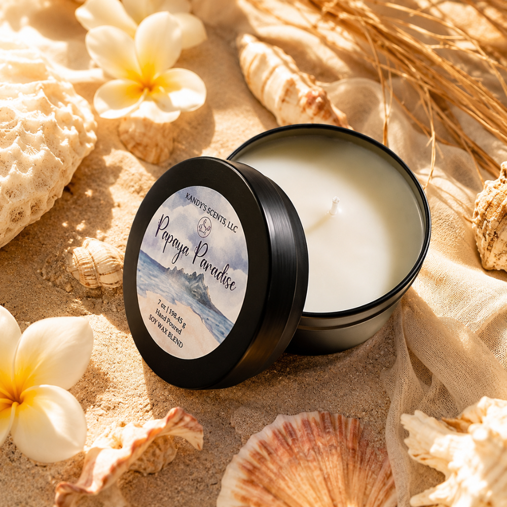 Candle in a black container with a decorative label on a sandy background with flowers and shells.