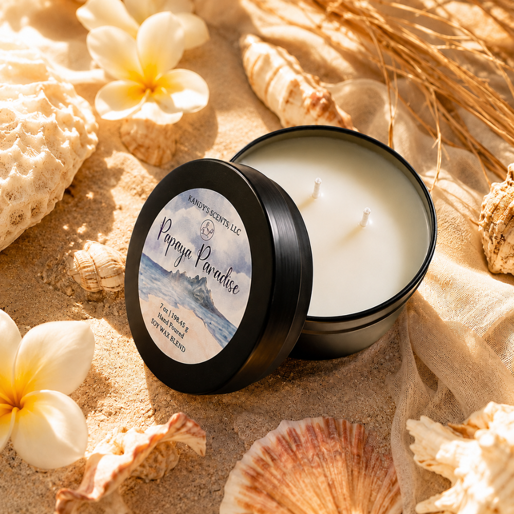 Candle in a tin labeled 'Papaya Paradise' surrounded by seashells and flowers on sand