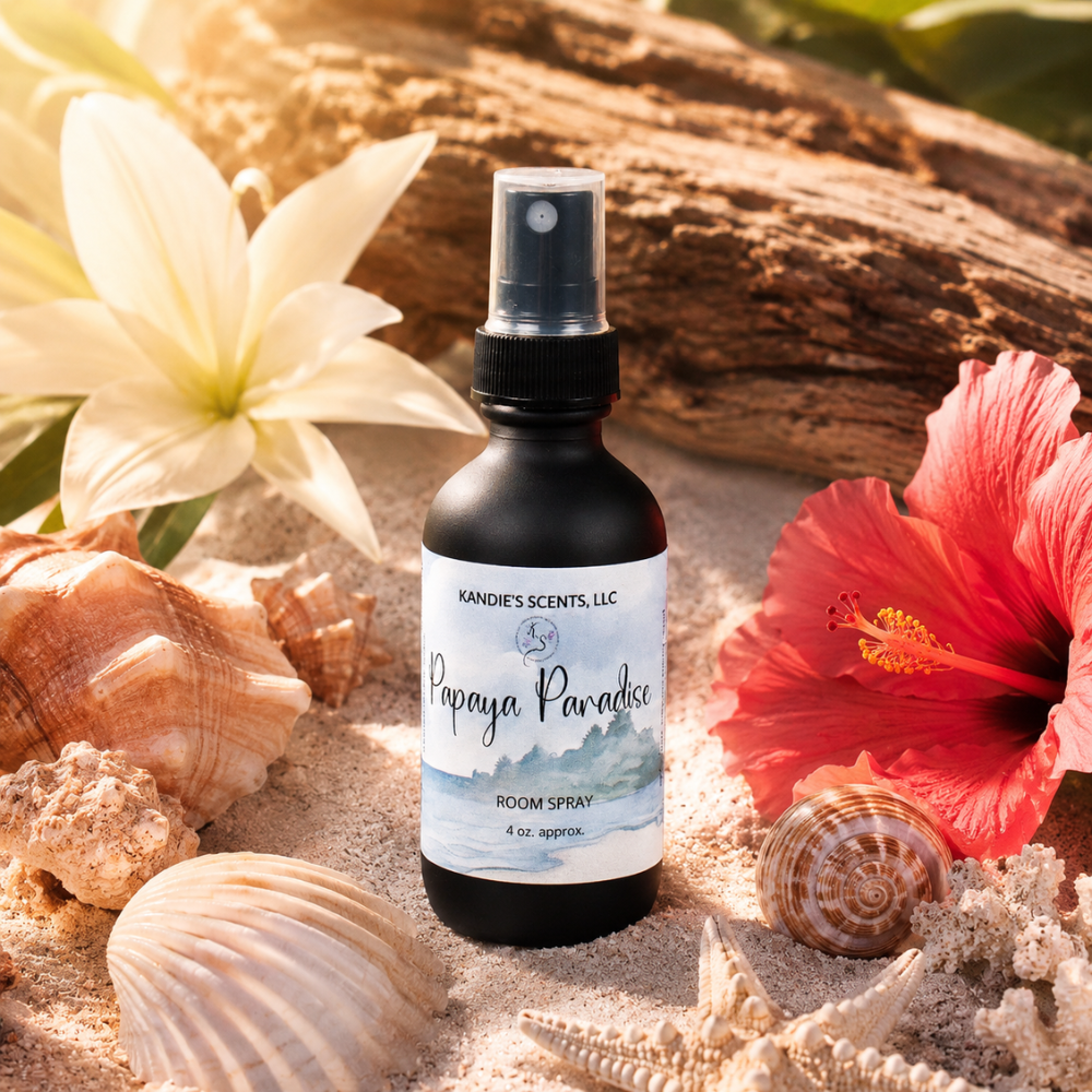 Room spray bottle labeled 'Papaya Paradise' surrounded by seashells and flowers on sand