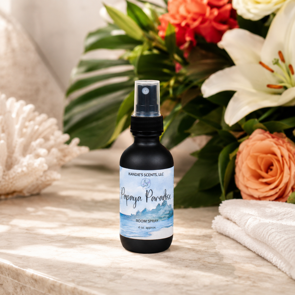 Room spray bottle labeled 'Papaya Paradise' on a wooden surface with flowers and towels in the background
