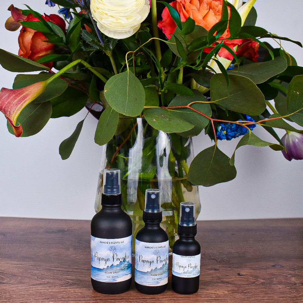 Three black bottles with labels in front of a vase of colorful flowers on a wooden surface.