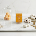 Wax melts packaging on a marble surface with cotton and a glass cloche.