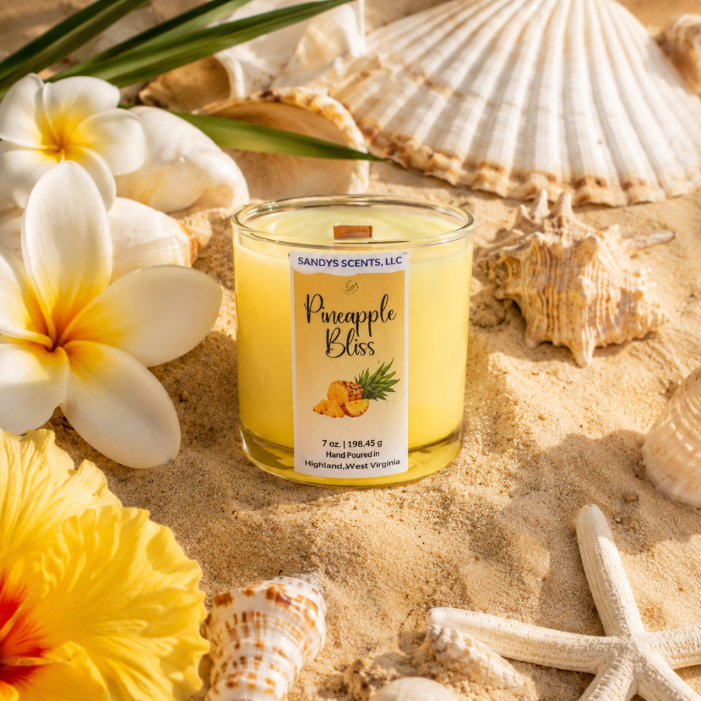 Scented candle labeled 'Pineapple Bliss' surrounded by seashells and flowers on sand