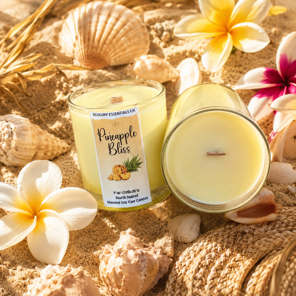 Two candles labeled 'Pineapple Bliss' on sand with flowers and shells