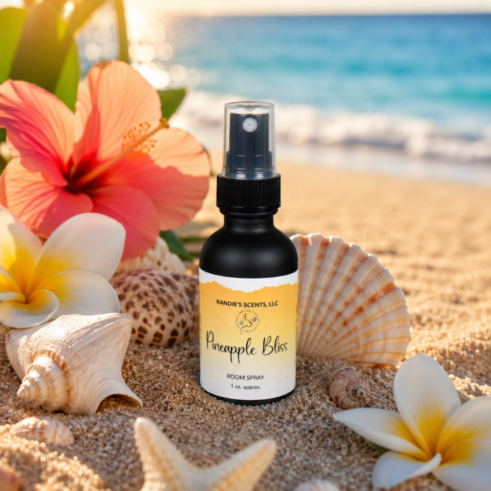Room spray bottle labeled 'Pineapple Bliss' on a sandy beach with flowers and shells.