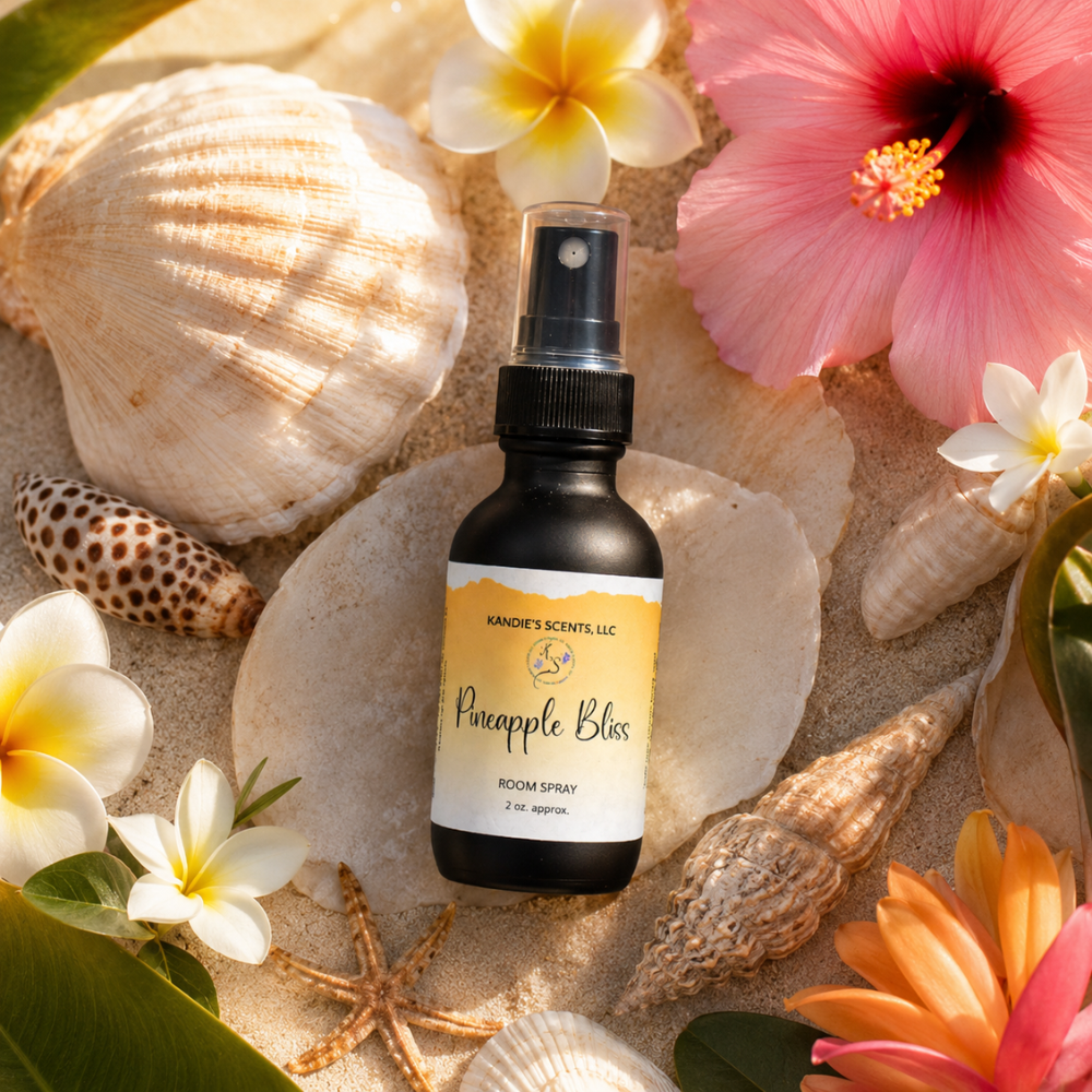 Room spray bottle labeled 'Pineapple Bliss' surrounded by seashells and flowers on sand