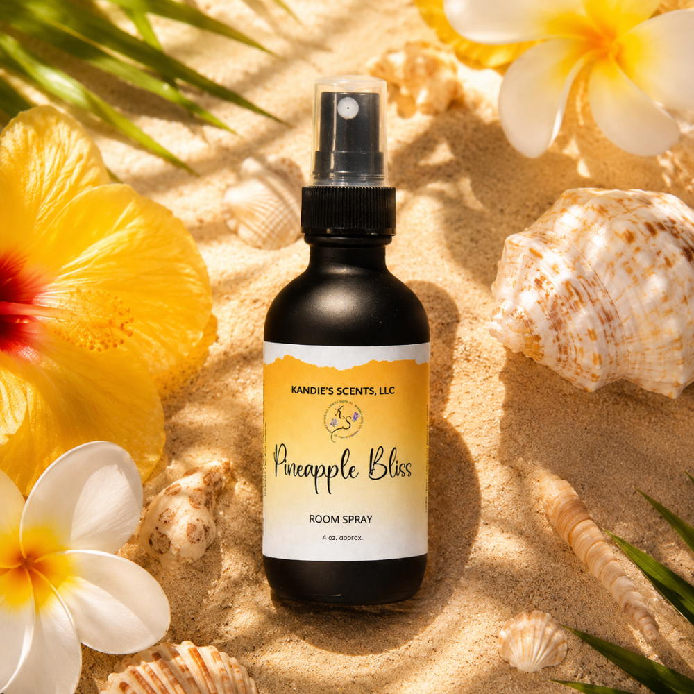 Room spray bottle labeled 'Pineapple Bliss' surrounded by tropical flowers and shells on sand