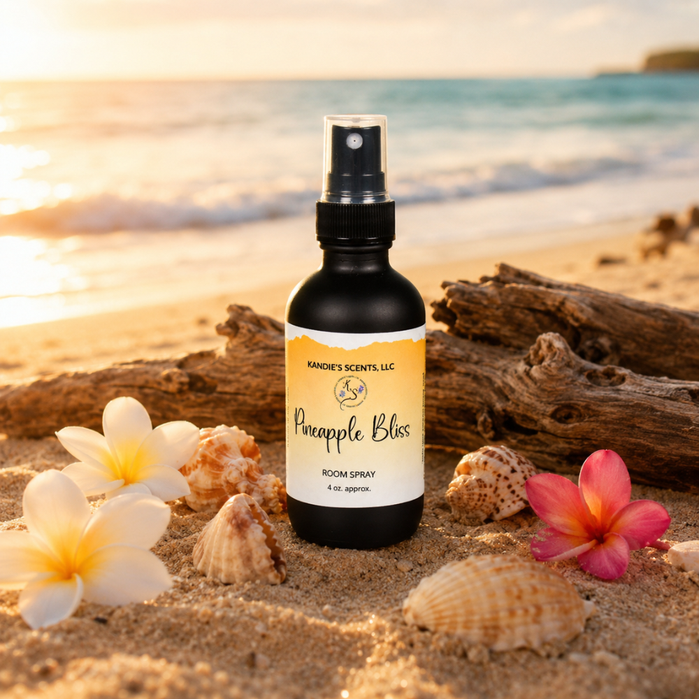 Room spray bottle labeled 'Pineapple Bliss' on a beach with flowers and driftwood.