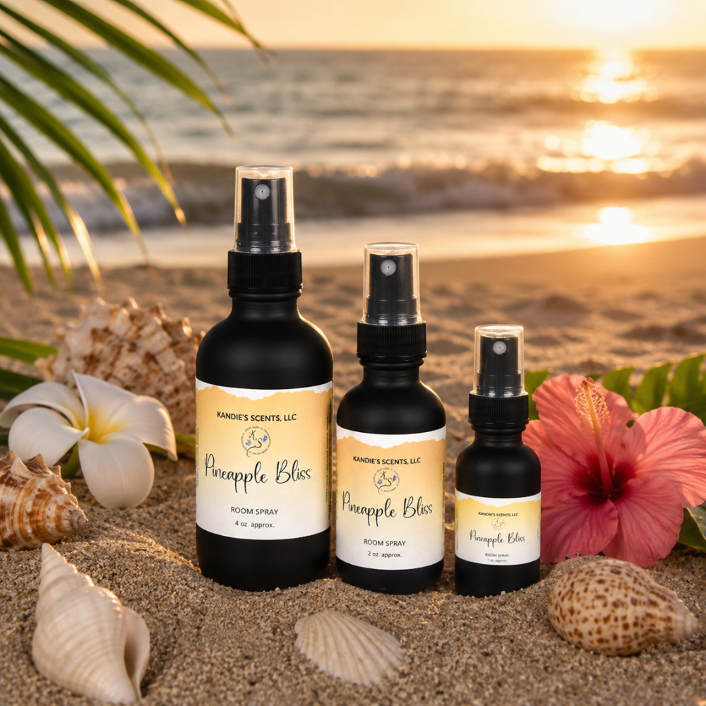Three bottles of 'Pineapple Bliss' room spray on a sandy beach with flowers and shells.