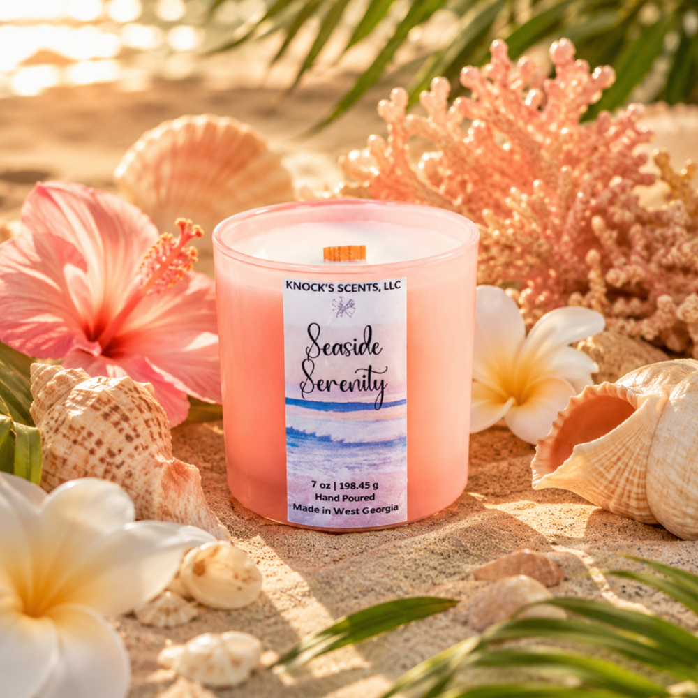 Candle labeled 'Seaside Serenity' surrounded by flowers and shells on a sandy surface