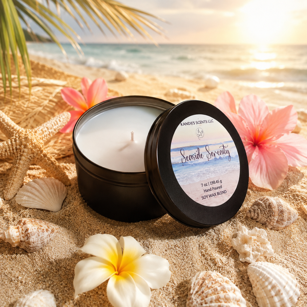 Candle in a black tin labeled 'Seaside Serenity' on sand with flowers and shells