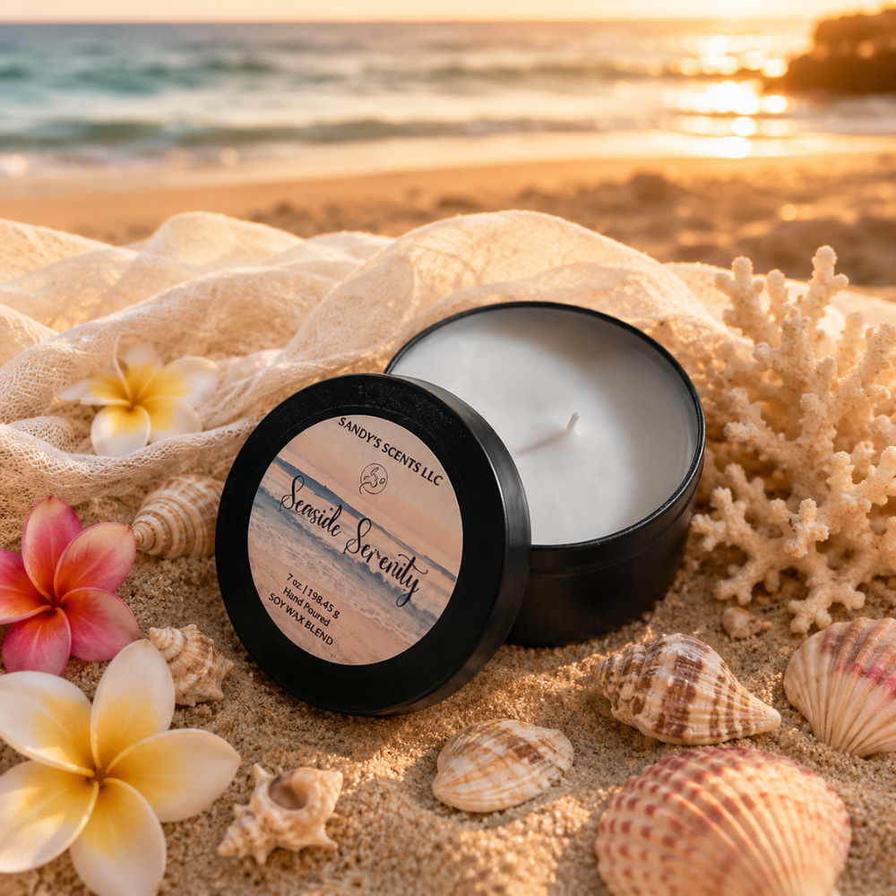 Scented candle in a black container on a sandy beach with flowers and shells.