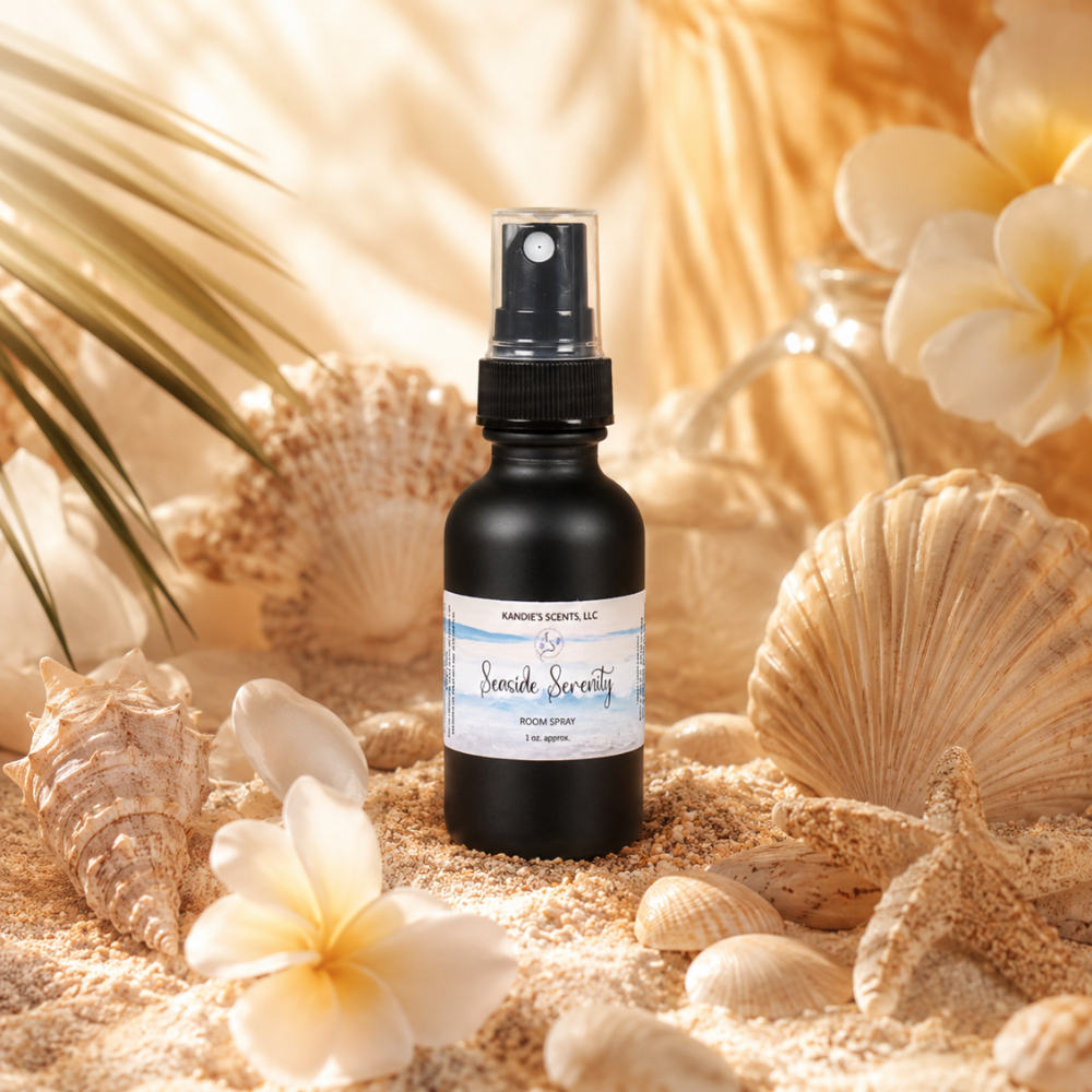 Black spray bottle labeled 'Seaside Serenity' surrounded by seashells and flowers on sand