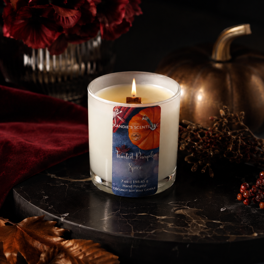 A lit hand-poured scented candle in a white glass jar sits on a dark marble surface. The label reads 'Kandie's Scents' and 'Toasted Pumpkin Spice.'