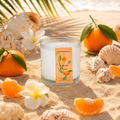 Candle with tangerine oil label surrounded by oranges, flowers, and shells on sand
