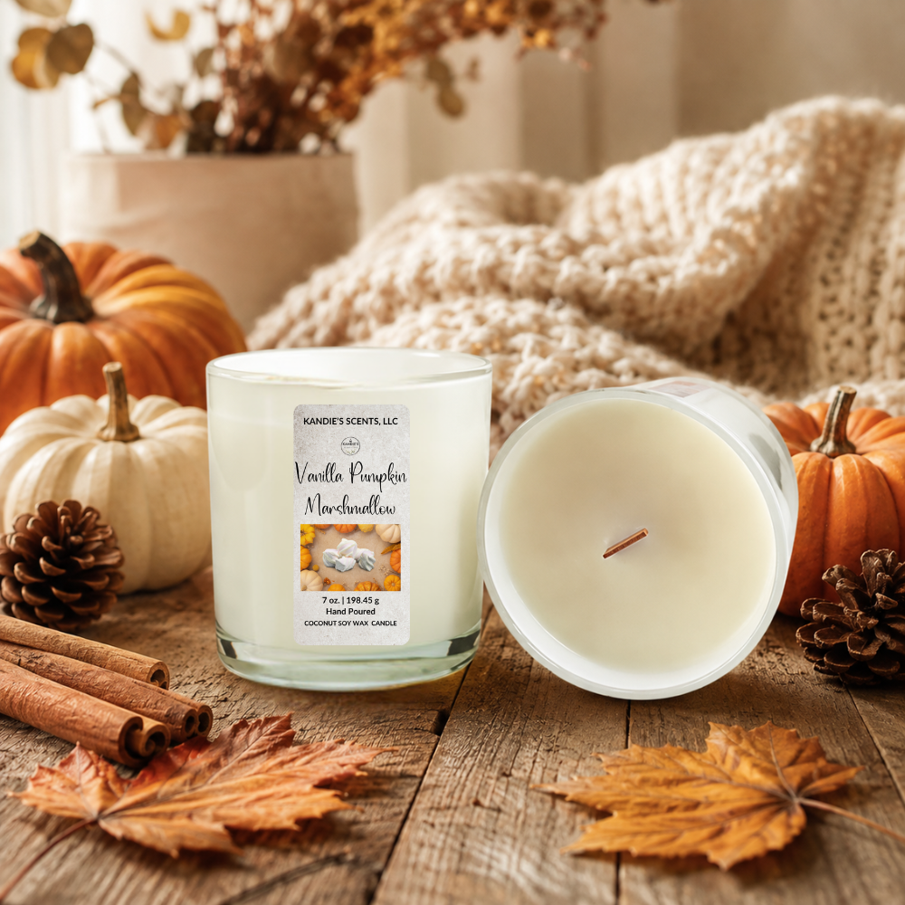 A scented candle in a white glass jar with white wax sits on a rustic wooden surface next to its lid, styled with pumpkins, pinecones, cinnamon sticks, and autumn leaves. A cozy cream knit blanket and dried floral arrangement are softly blurred in the background.