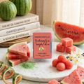 Kandie's Scents watermelon sugar glow wax melt with watermelon slices and books on a table.