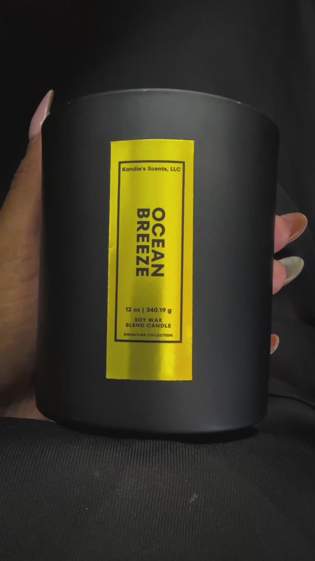 A slow-turn video of the 12 oz Ocean Breeze candle, cradled in one hand. The matte black jar with its tall, vertical gold foil label shimmers as it’s rotated, revealing the sleek, upscale branding of Kandie’s Scents. This premium candle embodies bold simplicity and timeless luxury.